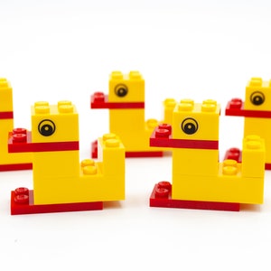 Könnte beinhalten: Fünf gelbe Plastik-Spielzeugenten mit roten Schnäbeln und schwarzen Augen. Die Enten sind aus Lego-Steinen gebaut und in einer Reihe angeordnet.