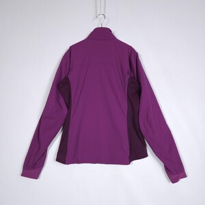 May include: A purple jacket with a full zipper and long sleeves. The jacket has a high collar and dark purple panels on the sides. The jacket is hanging on a metal hanger against a white background.