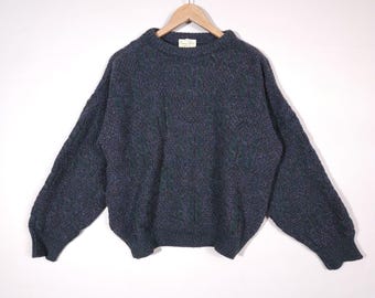 May include: A dark gray knitted sweater with a cable knit pattern. The sweater has long sleeves and a crew neck.