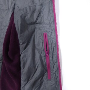 May include: Close-up of a gray jacket with a purple interior. The jacket has a magenta zipper and a matching magenta zipper pocket. The interior is a deep purple color.