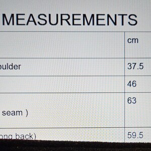 May include: A table of garment measurements in centimeters and inches. Measurements include shoulder to shoulder (14.7 in/37.5 cm), pit to pit (18 in/46 cm), sleeve length (24.7 in/63 cm), and total length (23.5 in/59.5 cm).
