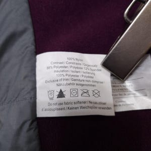 May include: Close-up of a white tag with black text detailing the composition of a garment. The tag includes fabric percentages, care instructions, and a warning against fabric softener. The background is a deep purple fabric.