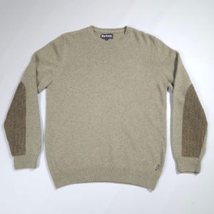 May include: A light brown crew neck sweater with brown elbow patches. The sweater has the brand name "Barbour" on the label. The sweater is made of a soft material.