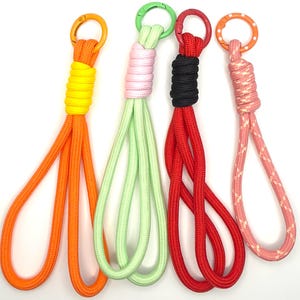 May include: Four colorful keychains with carabiner clips. The keychains feature orange, green, red, and pink rope loops. Each keychain has a different colored clip: orange, green, red, and orange. The rope is wrapped in a contrasting color at the top.