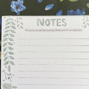 May include: A white notepad with a green floral border and the text "NOTES" in a light green font. The text "SOME DAYS I AM THE FLOWER. SOME DAYS I AM THE RAIN." is printed below the title.