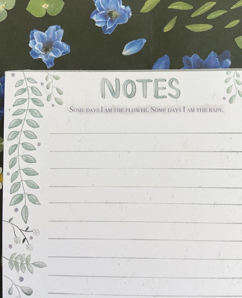 May include: A white notepad with a green floral border and the text "NOTES" in a light green font. The text "SOME DAYS I AM THE FLOWER. SOME DAYS I AM THE RAIN." is printed below the title.