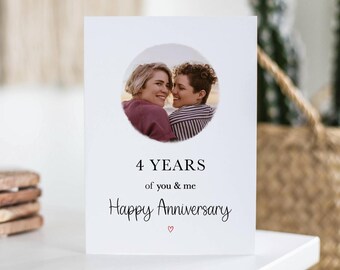 May include: A white greeting card with a circular photo of two people smiling. The card reads "4 YEARS of you & me Happy Anniversary" with a small red heart below.