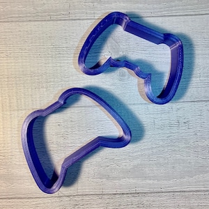May include: Two purple plastic cookie cutters shaped like video game controllers.