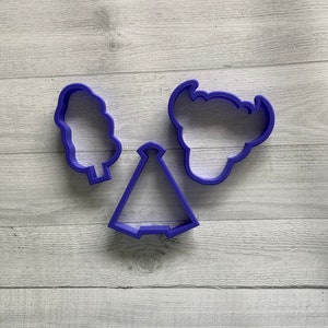 May include: Three purple plastic cookie cutters, shaped like a tree, a tent, and a bear head.