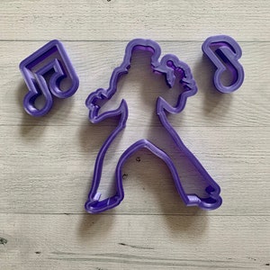 May include: Purple plastic cookie cutters in the shape of a person singing into a microphone and two treble clefs.