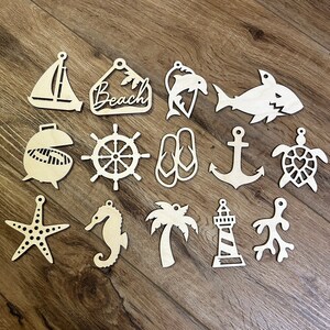 May include: A collection of unfinished wooden beach-themed cutouts. Designs include a sailboat, a sign that says "Beach", a dolphin, a shark, a grill, a ship's wheel, flip-flops, an anchor, a turtle, a starfish, a seahorse, a palm tree, a lighthouse, and coral.