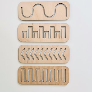 May include: Four wooden tracing boards with different patterns cut out. The patterns include a wavy line, a series of vertical lines, a row of left-facing arrows, and a zig-zag line.