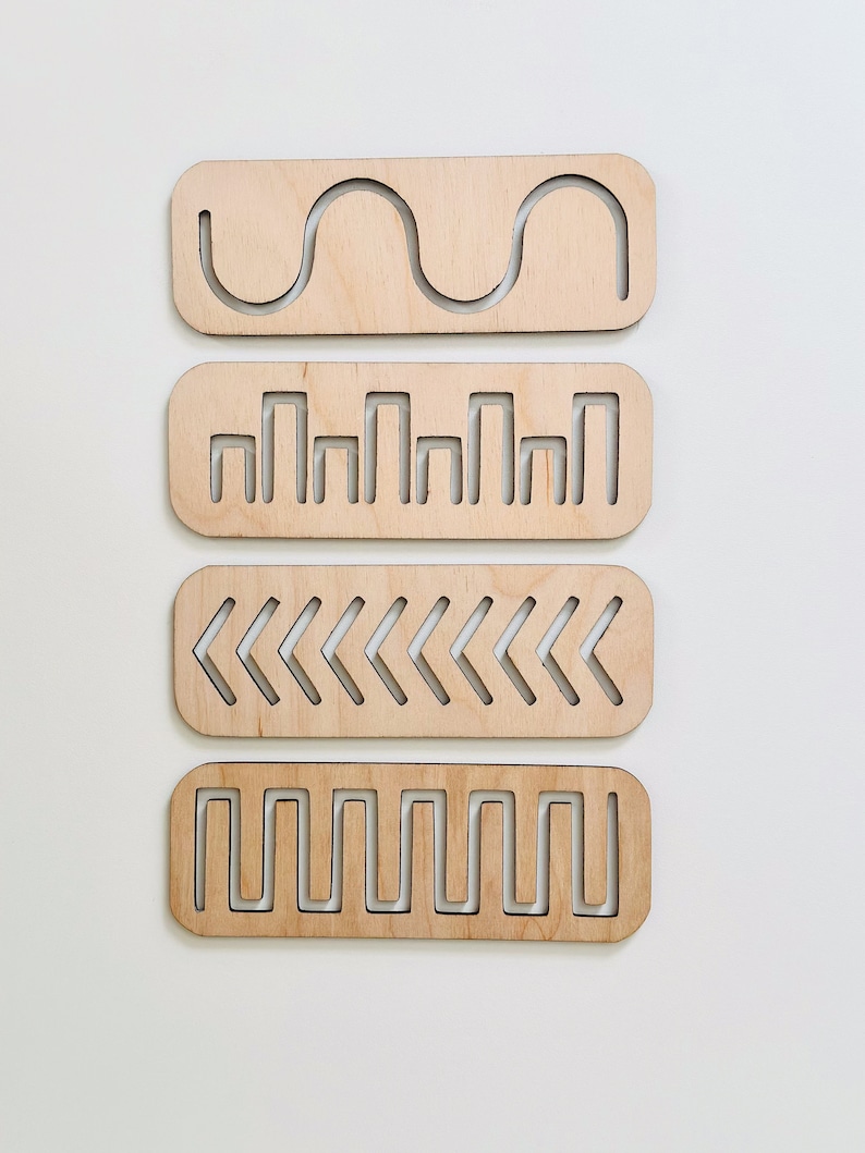 May include: Four wooden tracing boards with different patterns cut out. The patterns include a wavy line, a series of vertical lines, a row of left-facing arrows, and a zig-zag line.