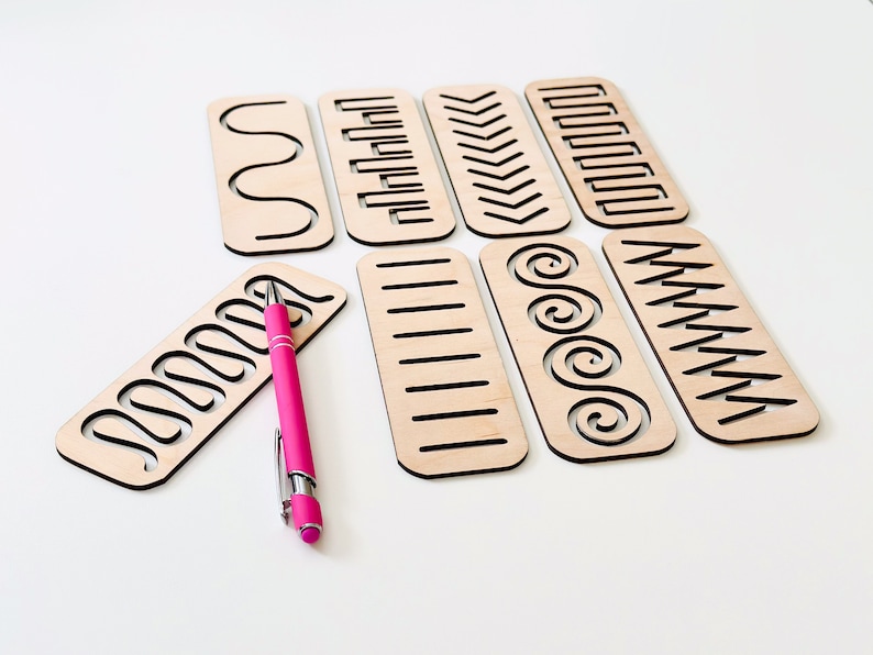 May include: Set of eight wooden stencils with different patterns, including wavy lines, zigzags, and spirals. A pink pen is lying next to the stencils.