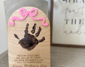May include: A wooden plaque with a handprint and a pink ribbon. The plaque has a message that reads "Hold my little hand and help me as I grow. You mean the world to me. I hope you always know. Happy Mother's Day. Love, Carson."