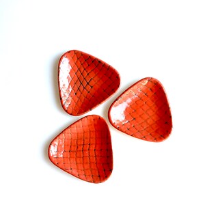 May include: Three small, triangular ceramic dishes with a textured, orange-red glaze. The dishes are arranged in a triangular pattern.