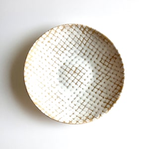 May include: A white ceramic bowl with a gold geometric pattern. The bowl is round and has a slightly raised rim.