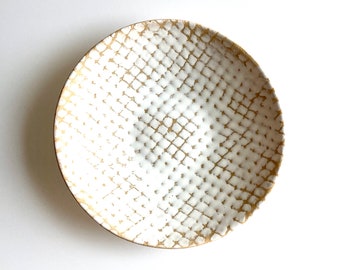 May include: A white ceramic bowl with a gold geometric pattern. The bowl is round and has a slightly raised rim.
