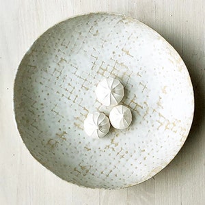 May include: A white ceramic bowl with a textured surface and a subtle gold glaze. The bowl is filled with four white meringue cookies.