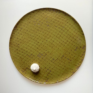 May include: A round, green ceramic plate with a textured surface. A single white meringue cookie sits on the plate.
