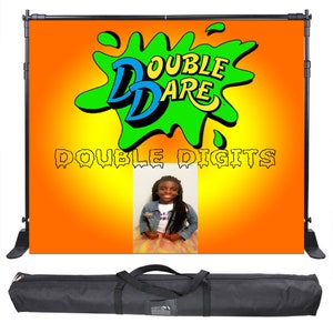 May include: A black backdrop stand with a bright orange background featuring a green slime splatter with the words "Double Dare" in blue and yellow letters. The words "Double Digits" are written in dripping green letters below the slime splatter. A photo of a young girl is in the lower right corner of the backdrop. The stand comes with a black carrying case.