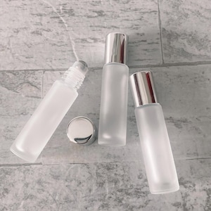 May include: Three frosted glass roller bottles with silver caps. The bottles are empty and ready to be filled with essential oils or other liquids.