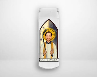 May include: A glass candle holder with a white background and a colourful image of a person holding a hockey stick. The image is in a stained glass style and has the text "SAINT PASTA" at the bottom.