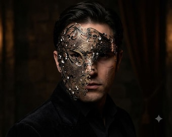May include: A metallic, filigree-style masquerade mask covering the left side of the face. The mask features an intricate, laser-cut scrollwork pattern in a dark bronze finish, accented with numerous small, clear, sparkling crystals throughout.
