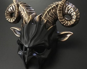 May include: A black and bronze mask with large, curved horns and pointed ears. The mask has a detailed, textured surface and a stylized design, likely for costume or decorative purposes. The horns are a contrasting bronze color.