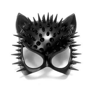 Puede incluir: M&aacute;scara negra con forma de ojo de gato con orejas puntiagudas y numerosas p&uacute;as negras. La m&aacute;scara tiene aberturas para los ojos y est&aacute; hecha de un material liso y brillante. Las p&uacute;as est&aacute;n espaciadas uniformemente.