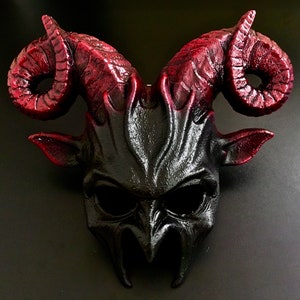 May include: A black and red devil mask with horns. The mask has a detailed, textured design and a menacing expression.