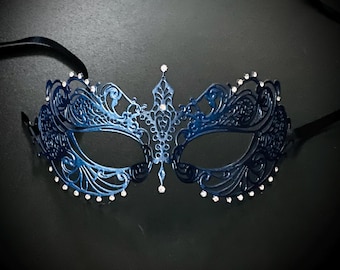 May include: A blue masquerade mask with intricate cutouts and rhinestones. The mask has a delicate, feminine design.