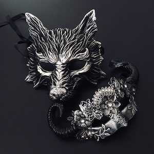 May include: A pair of masquerade masks, one is a wolf with silver and black fur, the other is a floral design with silver and black accents.