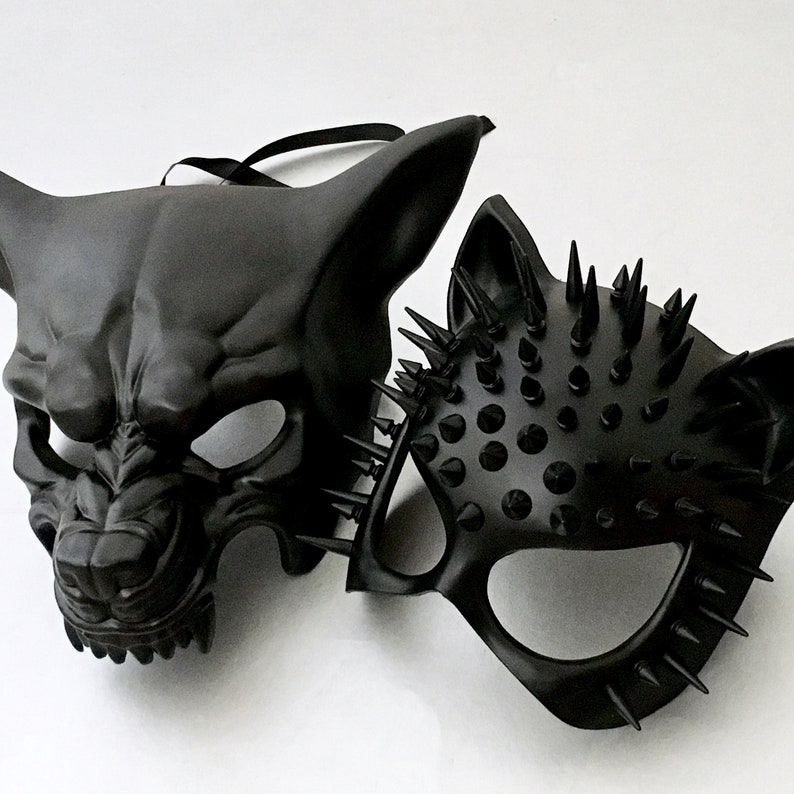 Puede incluir: Dos m&aacute;scaras negras. Una es una m&aacute;scara facial completa con un dise&ntilde;o feroz y animalista. La otra es una media m&aacute;scara con p&uacute;as afiladas. Ambas m&aacute;scaras tienen un acabado mate y probablemente sean para uso de vestuario o teatral.