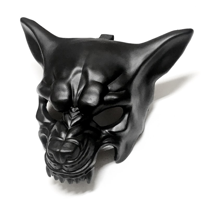Puede incluir: Una m&aacute;scara de pl&aacute;stico negro moldeado con forma de lobo o perro gru&ntilde;endo. La m&aacute;scara tiene orejas puntiagudas, un hocico detallado y aberturas para los ojos. Se adjunta una correa negra para usarla.