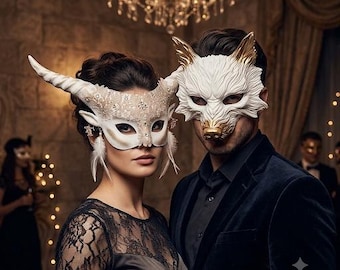 Könnte beinhalten: Zwei Maskenballmasken, getragen von Personen. Eine ist eine weiße, gehörnte Maske mit Spitzenverzierungen und weißen Federn. Die andere ist eine weiße, wolfsförmige Maske mit goldfarbenen Ohren und Nase. Beide tragen formelle Kleidung in dunkler Umgebung.