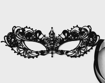 May include: A black lace masquerade mask featuring intricate filigree patterns and small, clear embedded rhinestones. The mask has a pointed center detail and includes long black ribbon ties on the right side for securing the item in place.