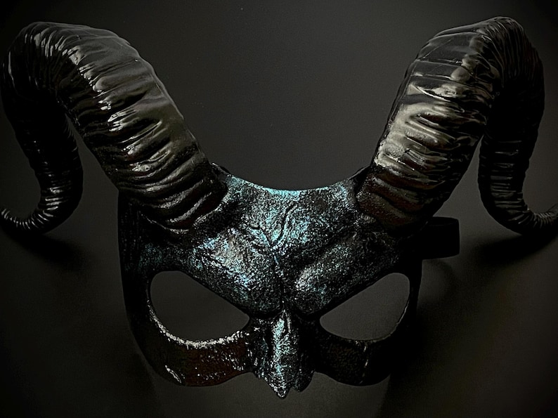 May include: A black horned mask with a textured finish and iridescent blue highlights. The mask features large, curved horns and eye openings, suitable for costume or theatrical use.