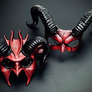 May include: Two red and black devil masks with horns. The masks have a textured, sculpted look and are made of leather.