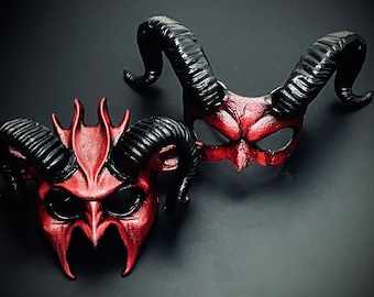 May include: Two red and black devil masks with horns. The masks have a textured, sculpted look and are made of leather.