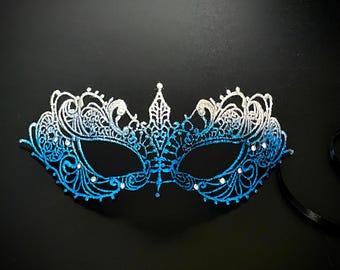 May include: A blue and silver masquerade mask with intricate lace detailing and rhinestones. The mask has a gradient effect, fading from silver to blue.
