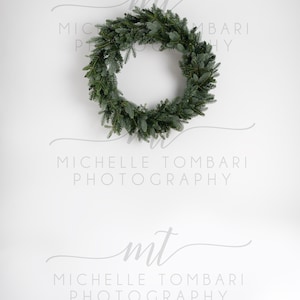 May include: A green evergreen wreath hangs on a white wall with the text "mt Michelle Tombari Photography" below it.