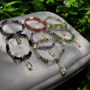 May include: Seven colorful beaded bracelets with a gold charm of the Virgin Mary. The bracelets are made with black, blue, red, purple, green, and clear beads.