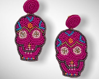 May include: A pair of pink beaded skull earrings with colorful details. The skulls are decorated with white, blue, orange, and gold beads.