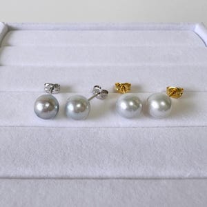 May include: Two pairs of stud earrings featuring spherical white pearls. One pair has silver-toned metal posts and butterfly backs, while the other pair features gold-toned metal posts and butterfly backs, all arranged in a horizontal row.