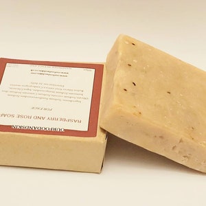 May include: A bar of OurFoodAndSkin Raspberry and Rose soap, packaged in a brown box with a red label. The label reads "OurFoodAndSkin", "Raspberry and Rose Soap", "For Face", and "Handmade in the USA".
