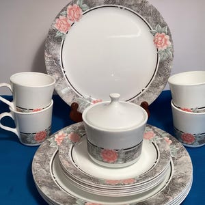May include: A complete white porcelain dinnerware set with a floral design. The set includes plates, saucers, cups, and a lidded sugar bowl. The plates and cups feature a gray border with pink roses.