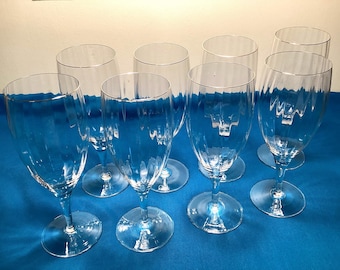 May include: Set of eight clear glass goblets with a ribbed design. The goblets are arranged on a blue surface.