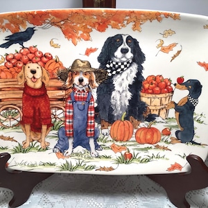 May include: A rectangular ceramic serving platter featuring a colorful illustration of four dogs in an autumn setting. The scene includes a wooden wagon filled with pumpkins and apples, falling orange leaves, and a black crow perched above.