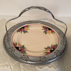 May include: A vintage silver serving tray with a cut-out design and a handle. The tray holds a cream-colored plate with a floral design in shades of red, orange, blue, and green.